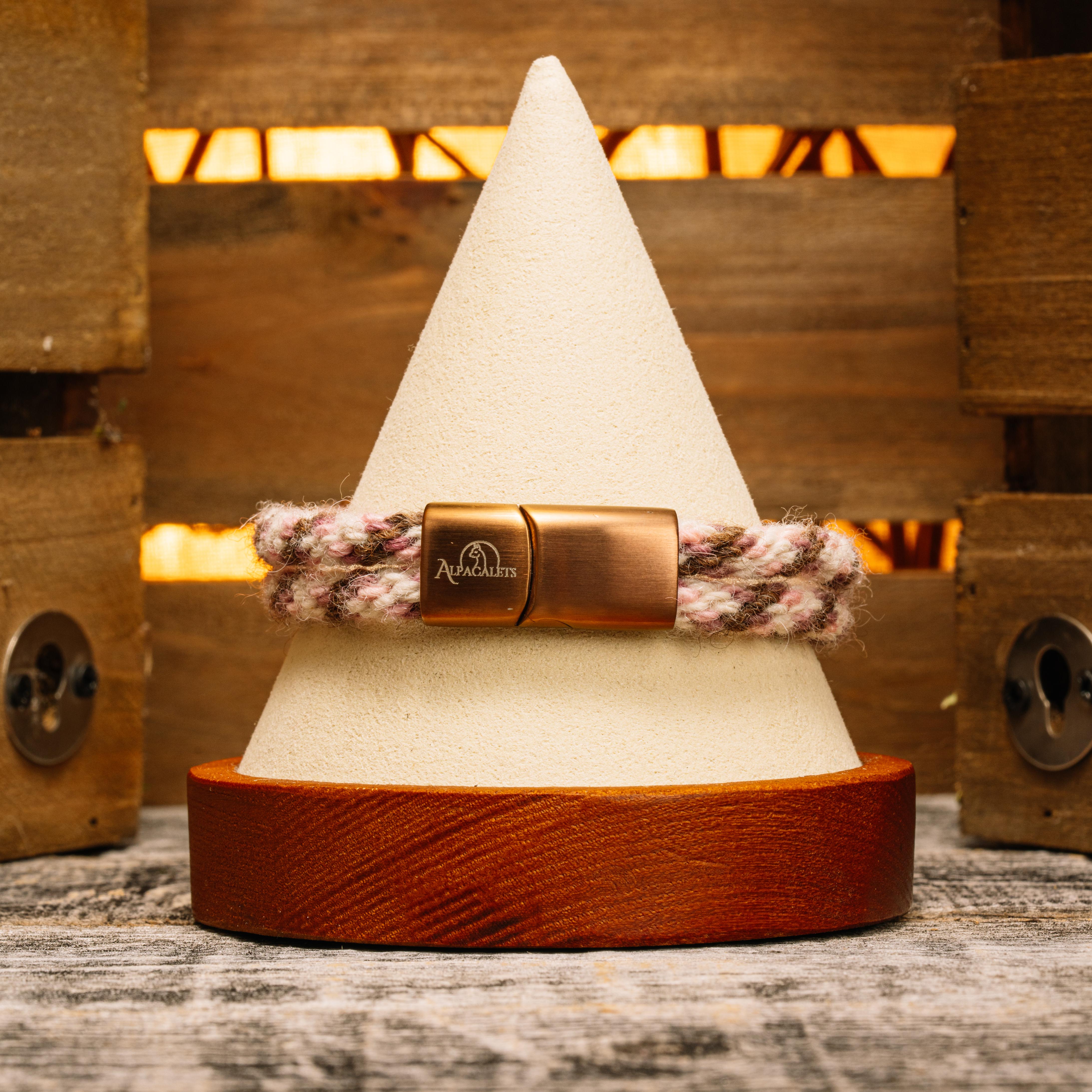 Bronze Blush Alpaca Bracelet displayed on a wooden pedestal, featuring soft rose, cream, and warm bronze tones.